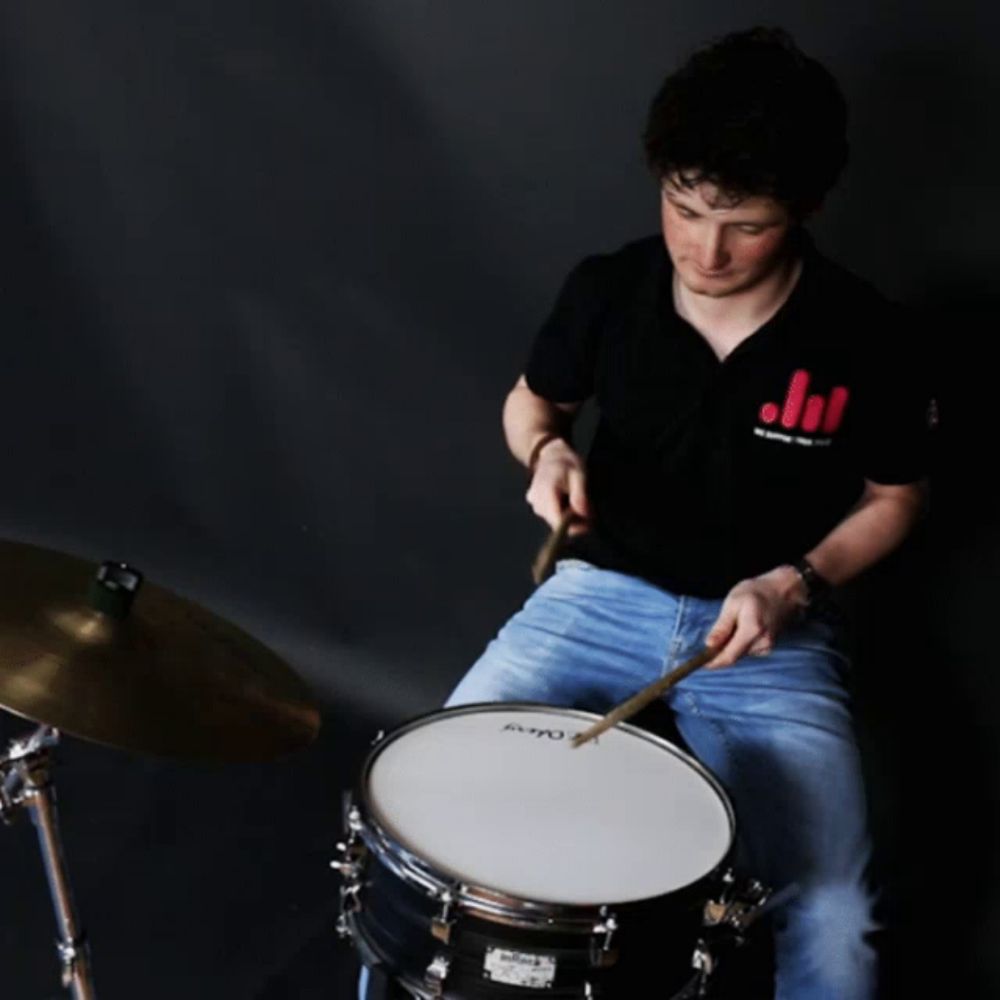 a young man is playing a drum with the name ba dumm behind him