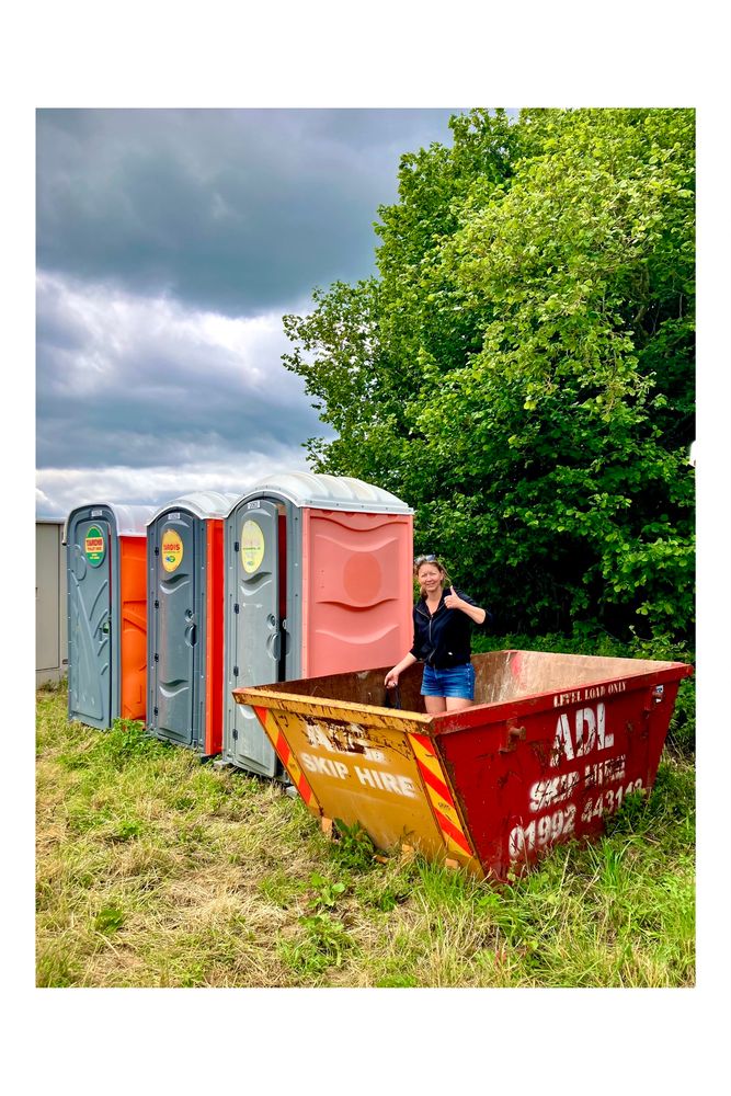 A member of the dig team cleaning out the slip on site next to a row of portaloos. The sky is very cloudy.