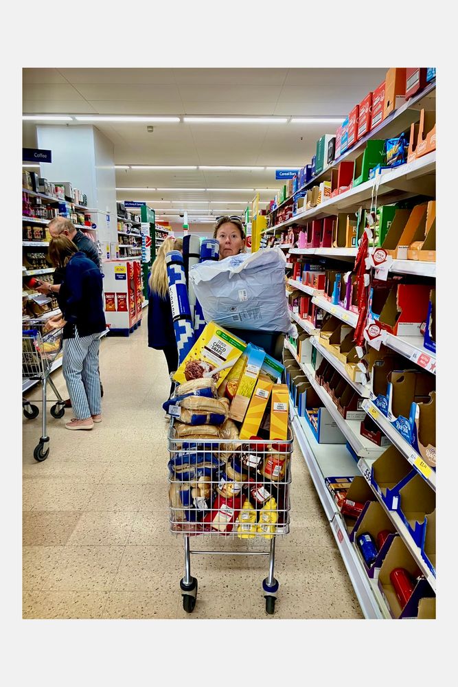 A member of the dig team in a supermarket with a full trolley of food and kit. You can just see their head.