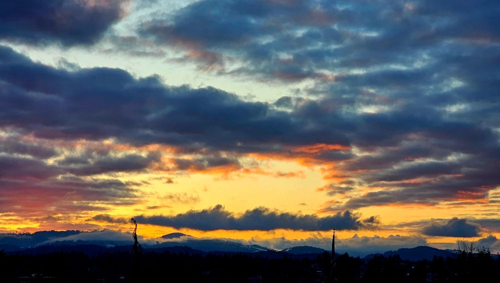 Sunrise over the far mountain ridge. The sky is has colors of yellows to some pinks and reds, with clouds