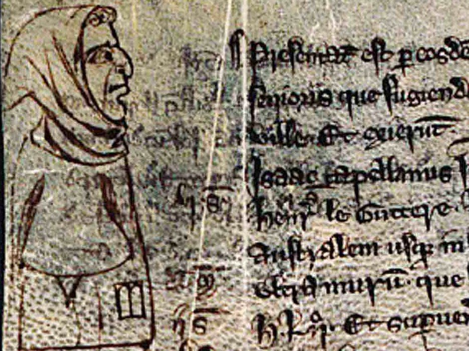 Section of a page from a medieval manuscript with Latin text (on the right). On the left, a marginal illustration: a male figure, shown in profile, is dressed in a hood, a small bit of curly hair stick out of the edge of the hood. He has a sloped, hooked nose. On his chest is the outline of a badge, shaped like the two tablets Moses carried.