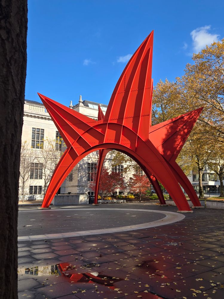 A large arched red-orange metal sculpture with spiky points like a stegosaurus.