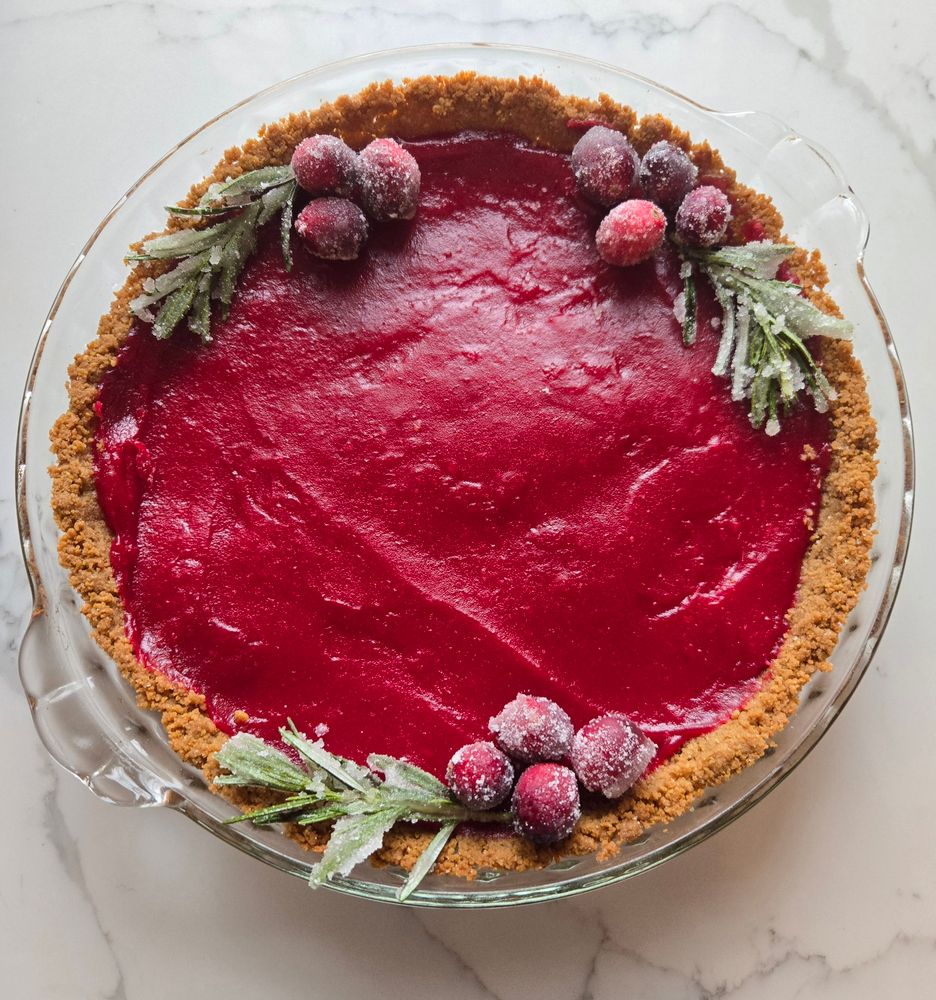 A bright dark pink curd tart with sugared cranberries and sugared rosemary decorations around the edge. 