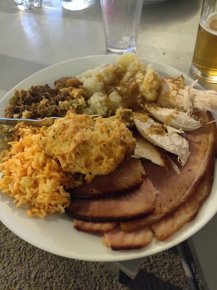 Thanksgiving spread of turkey, ham, mashed potatoes topped with gravy, rice with corn, stuffing, and a cheddar biscuit.