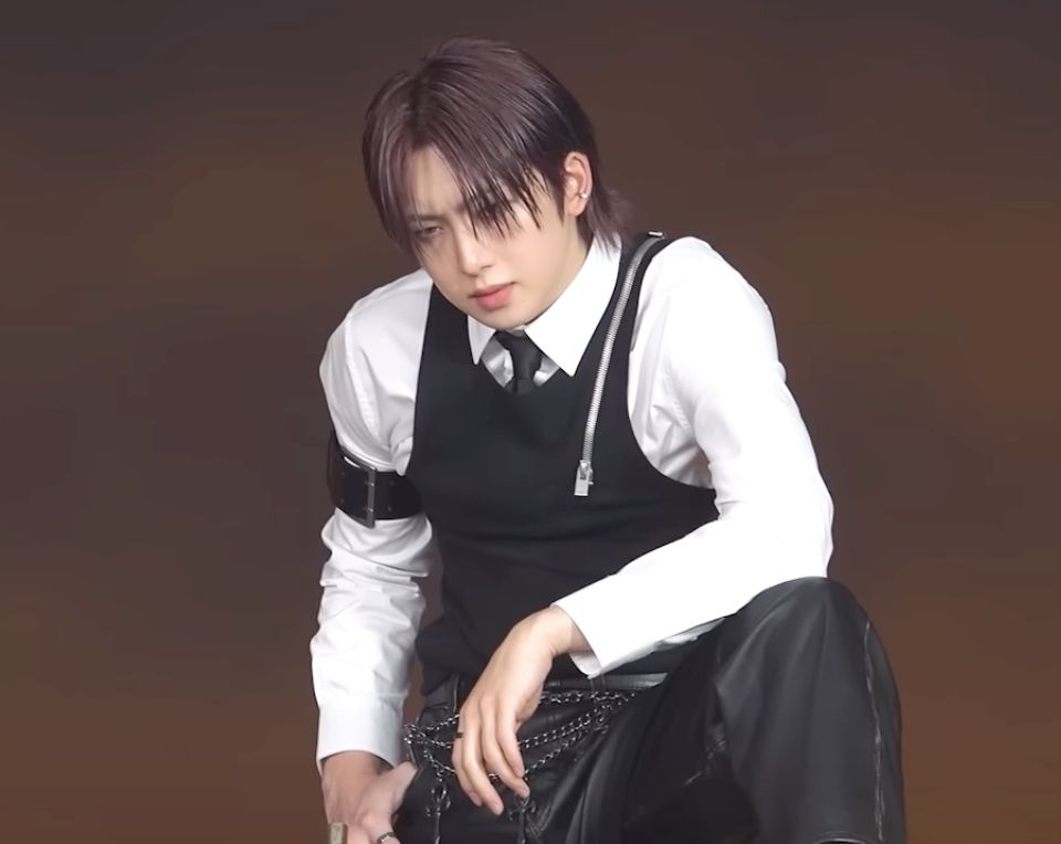 &Team Fuma standing with one foot propped on something. His elbow is on his knee and he has a thumb hitched into his pocket. 