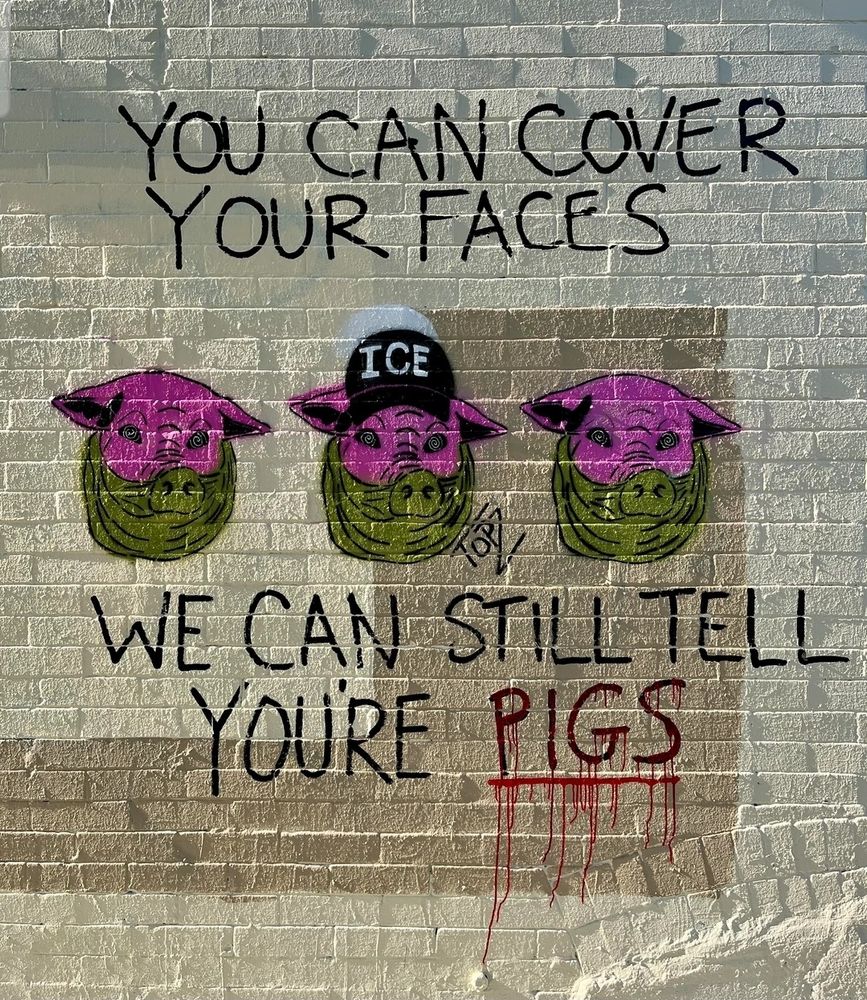 An ACAB street art piece. There are three pig heads in a row with text above and below them. They are depicted wearing green gaiter masks. The middle one has on an ICE baseball cap. The text reads "you can cover your faces. We can still tell you're pigs." Pigs is emphasized with red paint that is dripping down the wall to mimic blood.