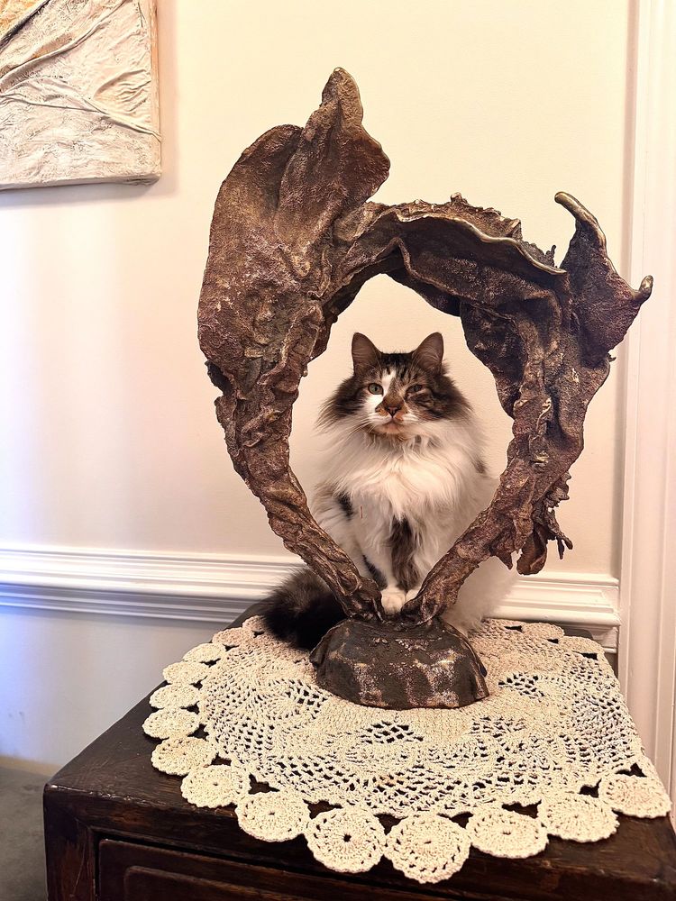 Fluffy cat sitting up inside bronze sculpture.