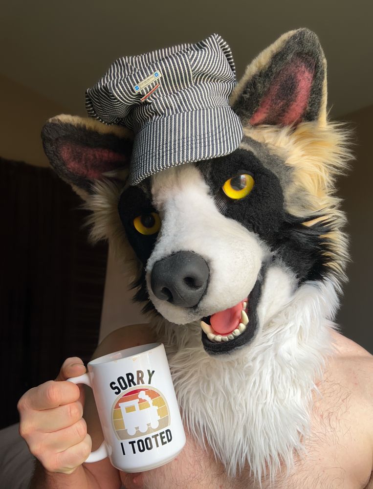 a male form holds up a mug which reads “sorry I tooted” with a silhouette of a train, wearing a cute, panda shepherd fursuit head 