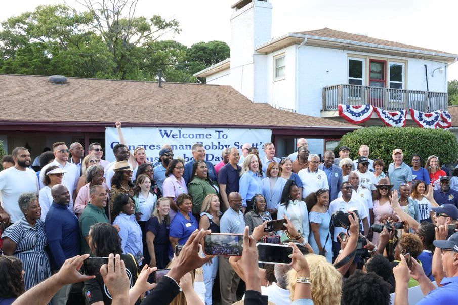 All elected officials and candidates attending pose for a picture in front of a house with the banner “Welcome to Congressman Bobby Scott’s Annual Labor Day Picnic” (partially obstructed).