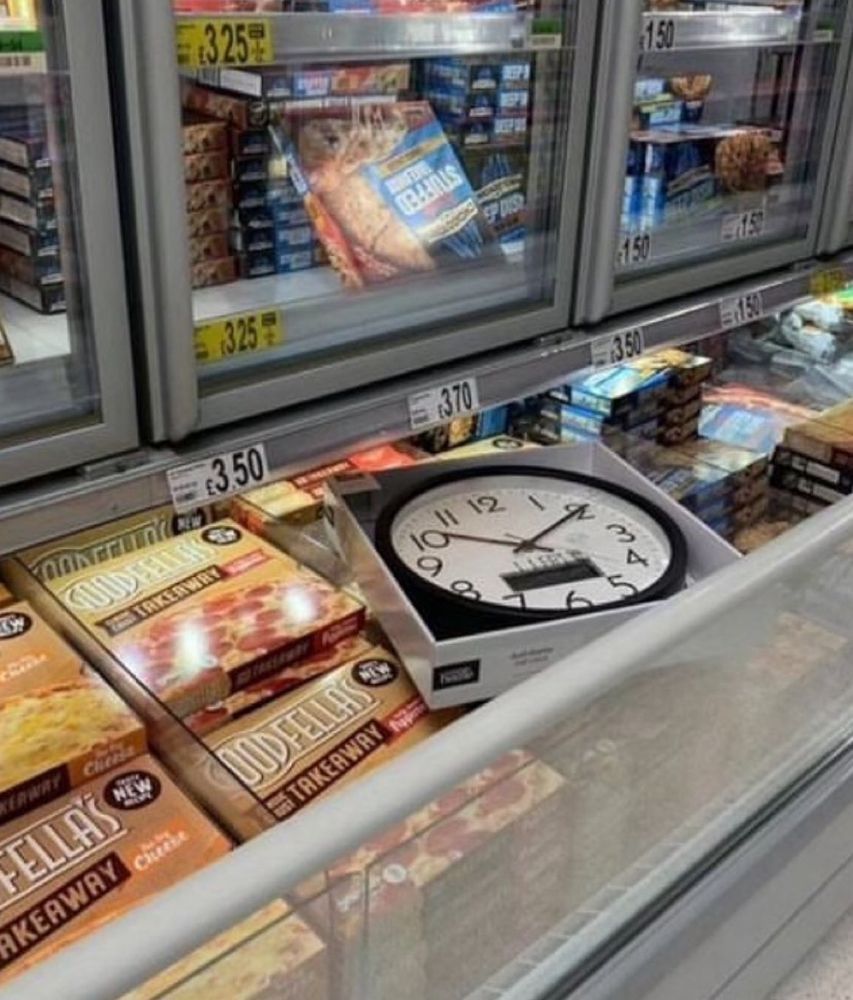A clock in a box in a freezer surrounded by pizzas 