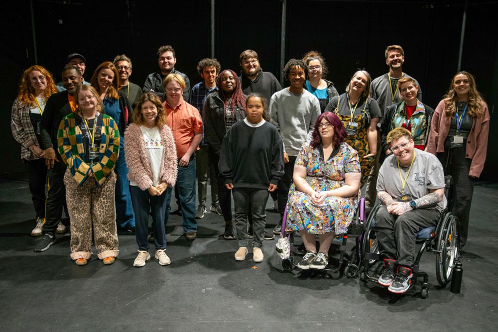 A large, diverse group of participants and organizers posing together on a stage with a black backdrop, celebrating a welcome evening. Everyone is looking at the camera and smiling.
