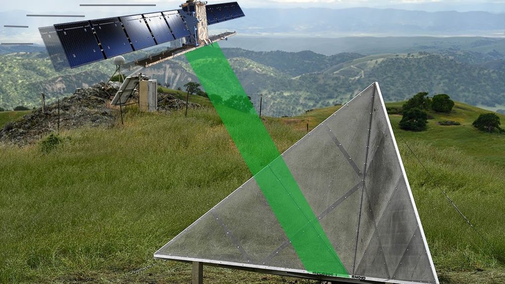 A silver, triangular corner reflector stands in a grassy field beneath a stylized satellite in orbit. A green radar beam connects the satellite to the reflector, illustrating signal reflection. Rolling hills and mountains appear in the background.