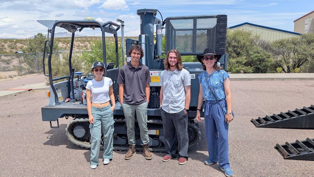 group of 4 interns stand in front of a weight-drop truck used for geophysical experiments