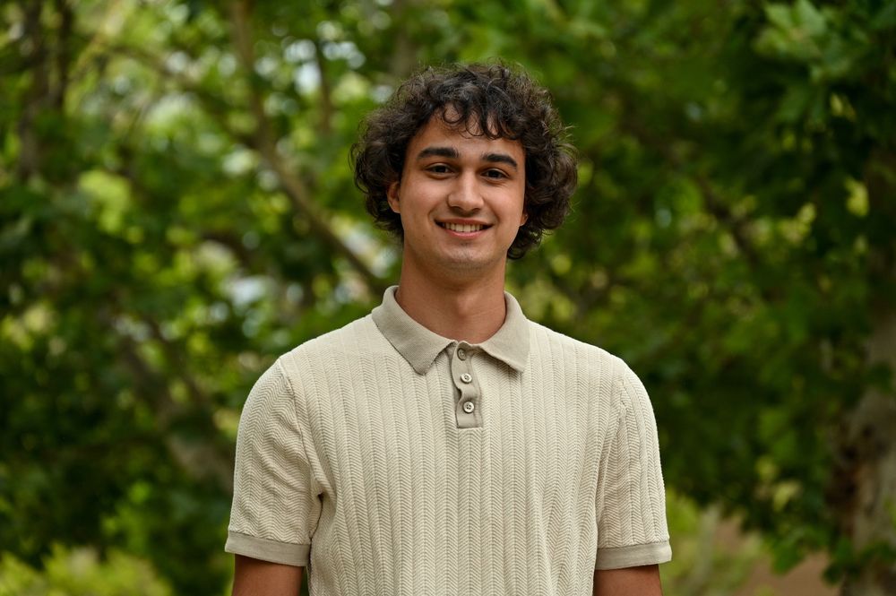 headshot of intern smiling at camera with green foliage in background