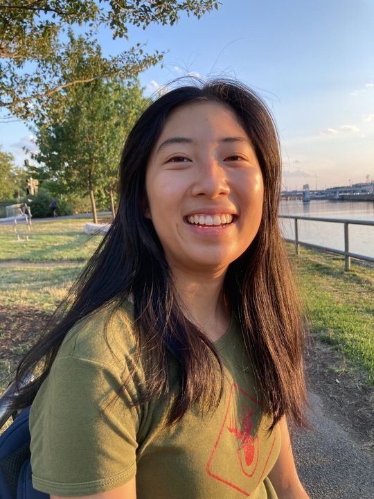 Head shot of Allison Wan, PhD student, wearing an olive shirt and sitting alongside a riverbank.