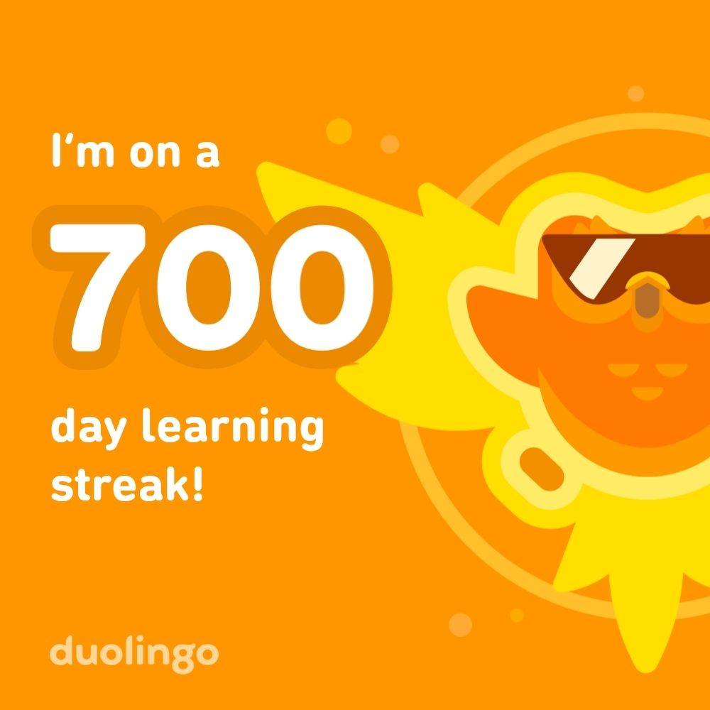 Vor orangem Hintergrund ist eine comic Eule zi sehen. Sie breitet vor stilisierten flammen die Flügel aus und trägt eine Sonnenbrille. Neben ihr ist zu lesen 'I'm on a 700 day learning streak! Duolingo" die Zahl 700 ist größer als der restliche Text. 