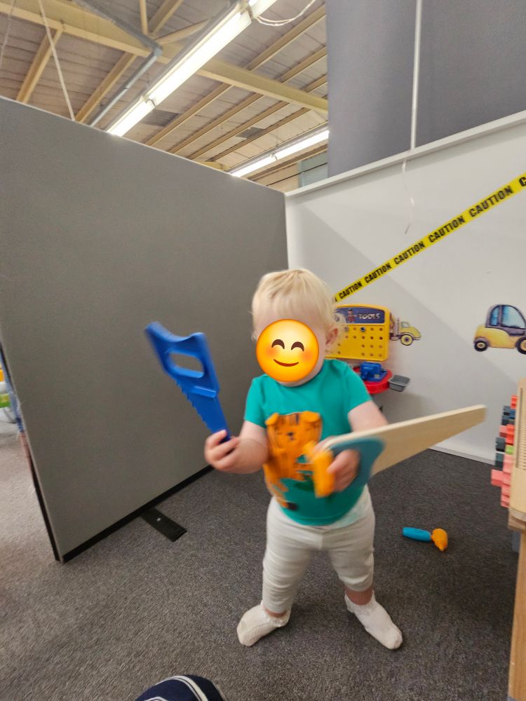 Small adorable baby toddling round carrying two wooden saws