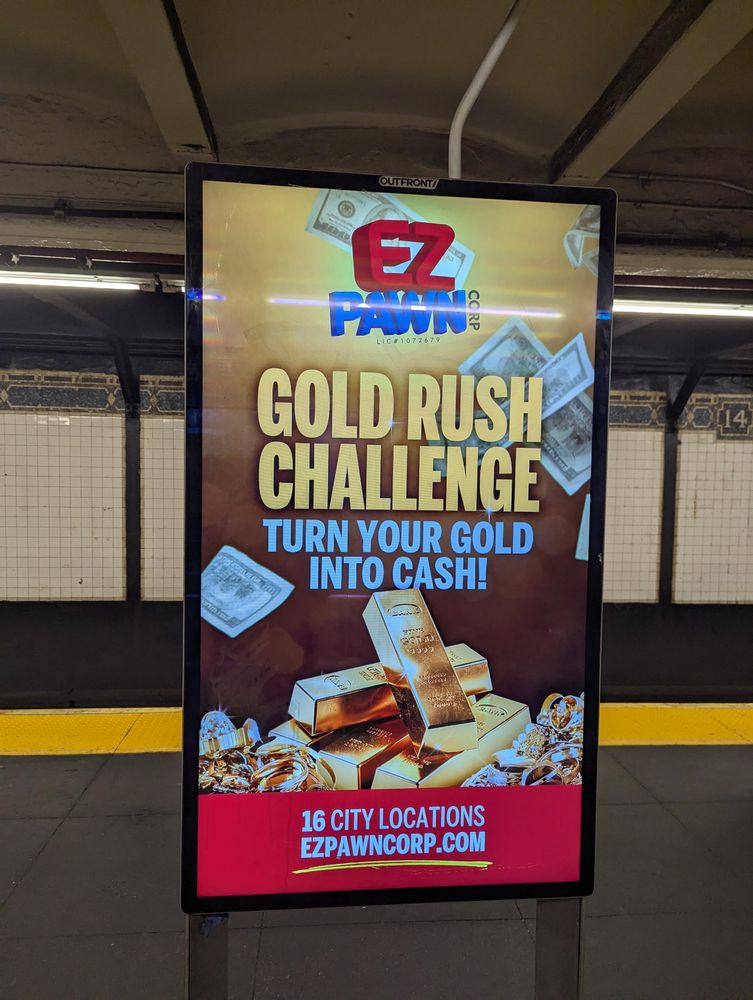 An electronic billboard ad on the NYC subway for ez pawn turn cash into gold. It's as garish and tacky as you expect. 
