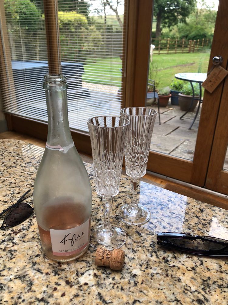 A marble working surface in a holiday apartment.  There’s a mostly-empty bottle of rose fizz, a couple of champagne flutes, and some sunglasses. 

Beyond, a grassy garden with hot tub is visible through the Venetian blinds. 