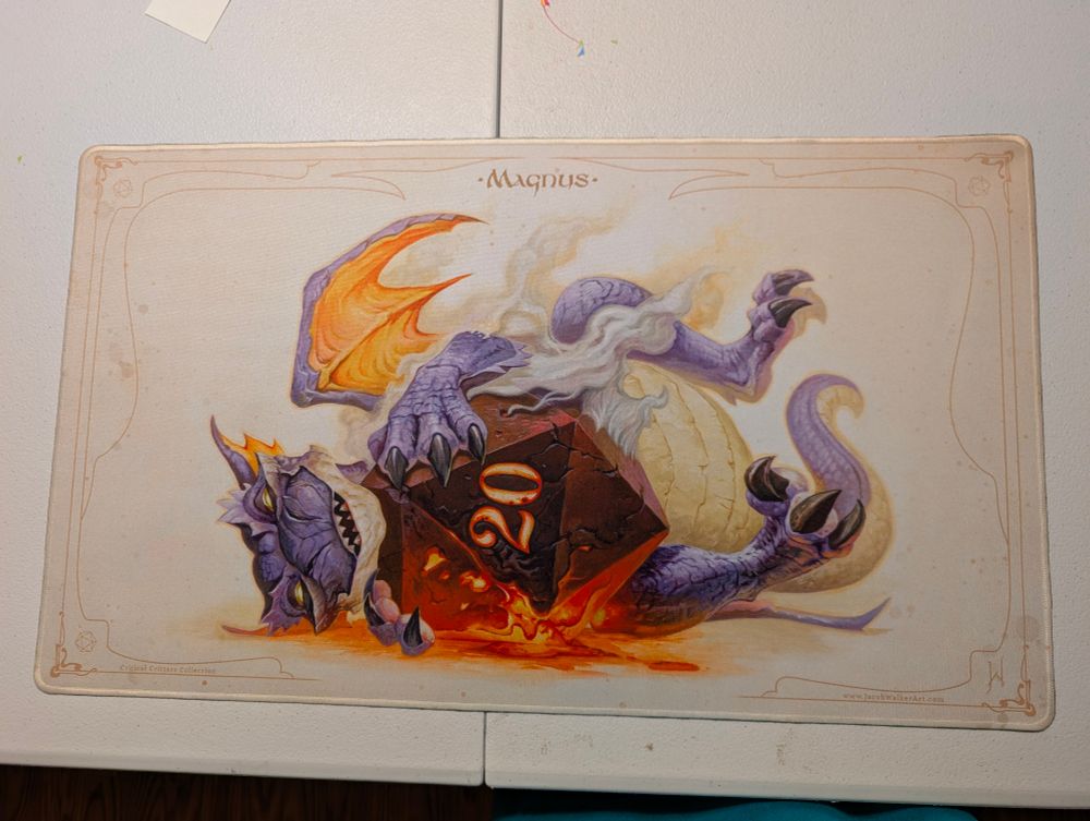 Dragon laying with a d20 on a gaming mat