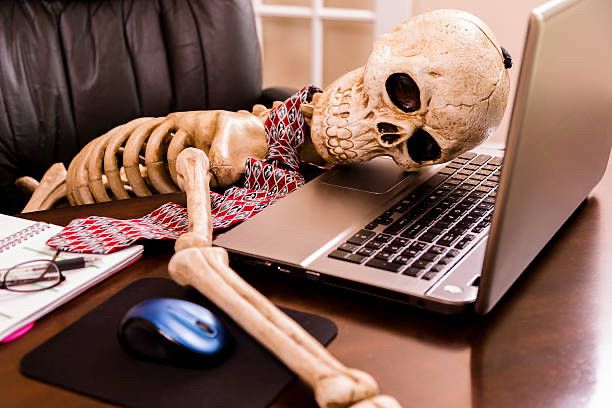 Skeleton with a tie face down on a laptop in a well lit office. 