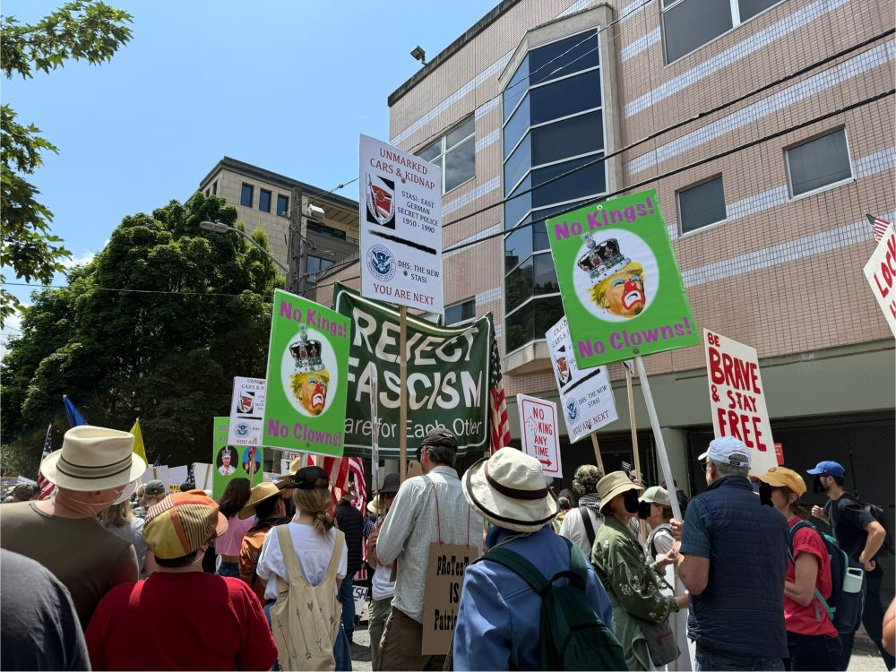 Photo from the No Kings protest in Seattle of marchers walking with signs saying “Reject Fascism” and “No Kings. No Clowns.”