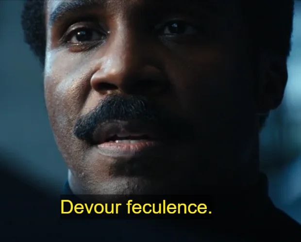 Close up of Mr. Milchick from Severance saying the words “Devour feculence”. 
