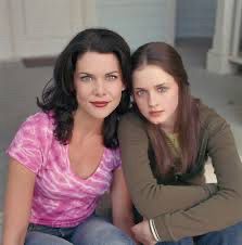 foto das gilmore girls: duas mulheres brancas, de cabelo escuro e olhos claros encarando a câmera. a da esquerda veste uma camiseta meio tie-dye rosa e branca e a da direita veste uma blusa de manga comprida marrom