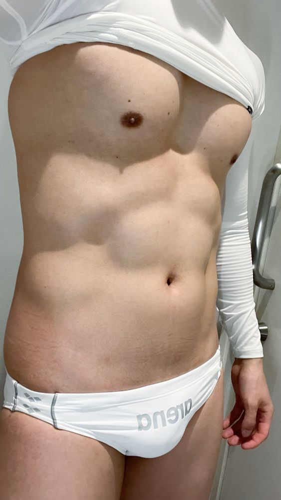 ジム更衣室にてインカメによる左右反転した自撮り。長袖コンプレッションをめくりあげて胸お腹を見せている。arenaの競パンを穿いている。