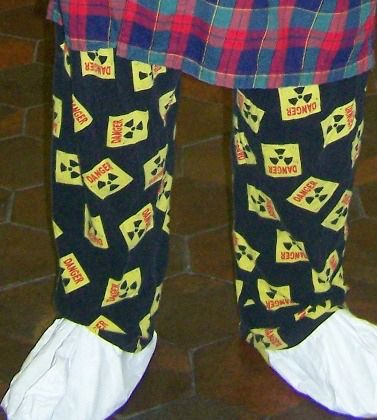 Closeup of black pajama trousers decorated with yellow and black radiation symbols and the word "Danger" in red. These are Bill Higgins's legs. On his feet are disposable white booties, or shoe covers, like those worn by workers to avoid contamination in radiation areas. Taken in Fermilab's Wilson Hall during the LHC Pajama Party in 2008. Photo copyright 2008 by William S. Higgins.