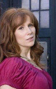 Catherine Tate's Donna Noble is stood in front of the TARDIS facing to her left, with her head turned towards the camera. She is wearing a pink top