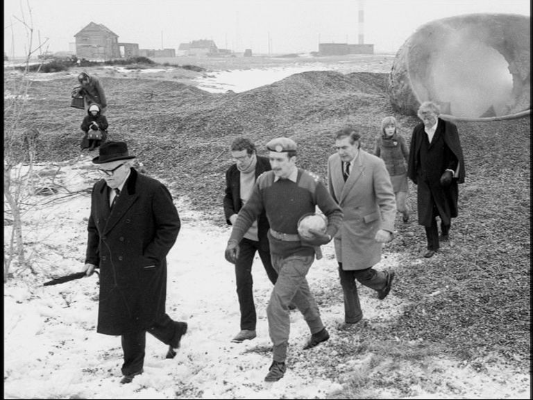 A black and white photo of The Doctor, Jo and UNIT leaving axos. The snow caused by it entering the atmosphere is still on the ground