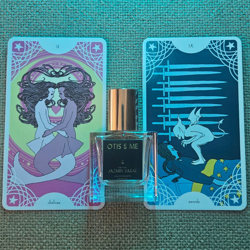 The II of Chalices and ghe IX of Swords tarot straddle a bottle of Otis & Me by Dana El Masri for Jazmin Saraï