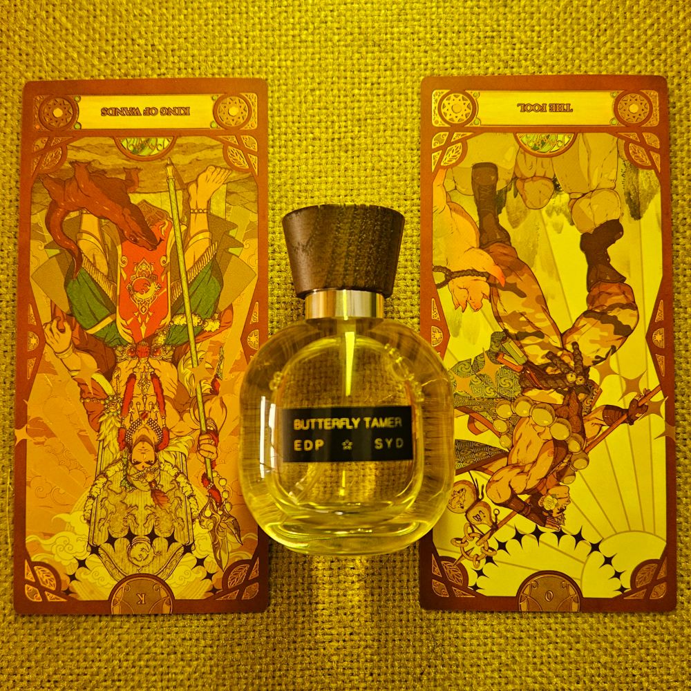 A reversed King of Wands and reversed card 0 the Fool straddle a bottle of Butterfly Tamer by Syd Buffman for Syd Botanica