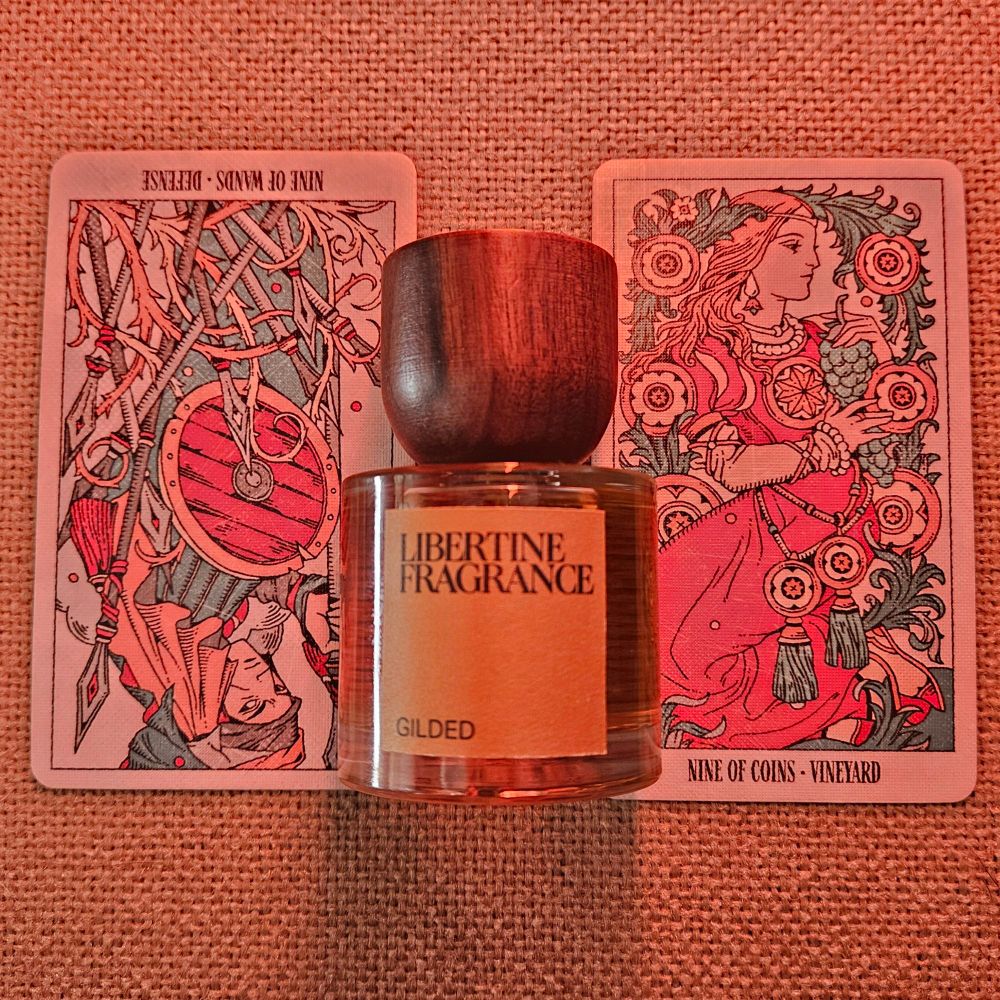 A reversed IX of Wands and upright IX of Coins straddle a bottle of Gilded, by Joshua Smith for Paraphrase Perfume