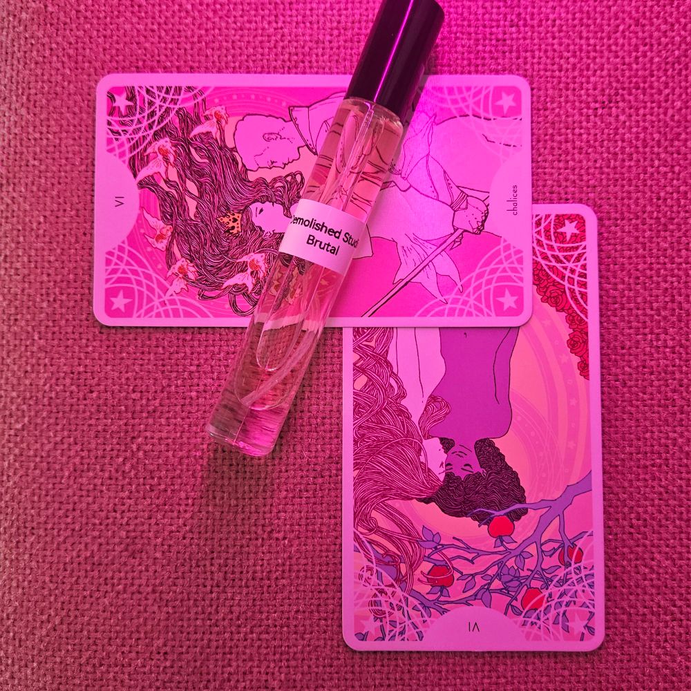 A reversed card VI the Lovers is topped by a VI of Chalices and a decant of Brutal by Demolished Studio