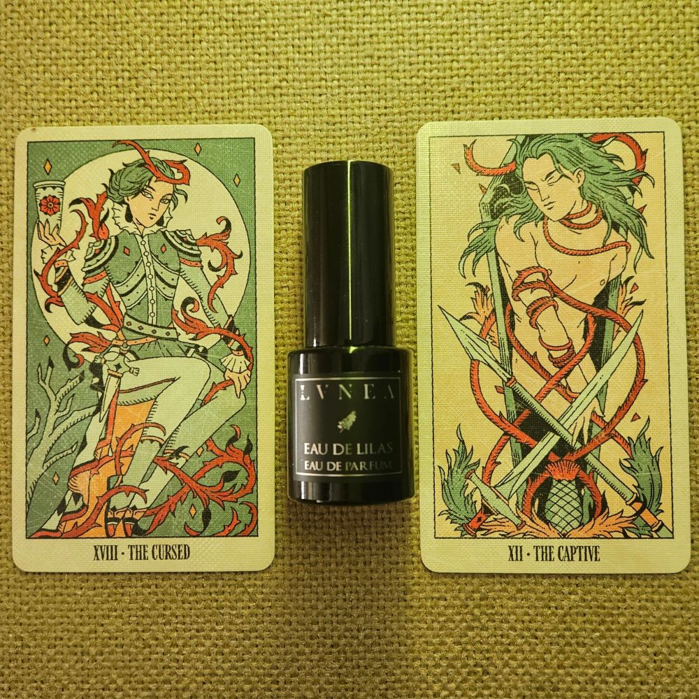 Card XVIII - the Cursed and Card XII - the Captive oracle straddle a bottle of Eau de Lilas by April Lea for LVNEA