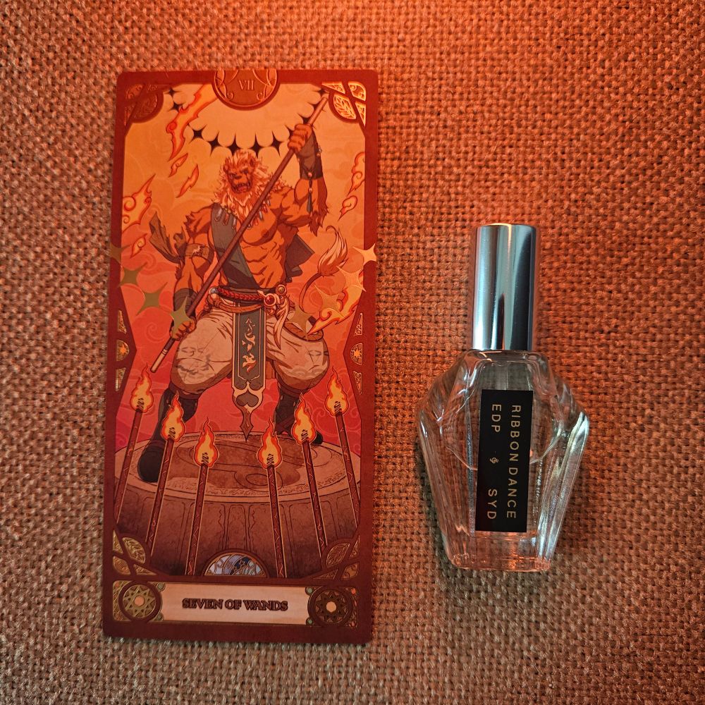 The VII of Wands tarot sits next to a bottle of Ribbon Dance by Syd Buffman for Syd Botanica