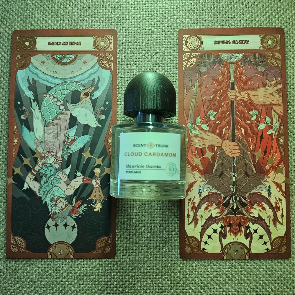 A reversed Page of Cups and reversed Ace of Wands tarot straddle a bottle of Cloud Cardamom by Mauricio Garcia for Scent Trunk