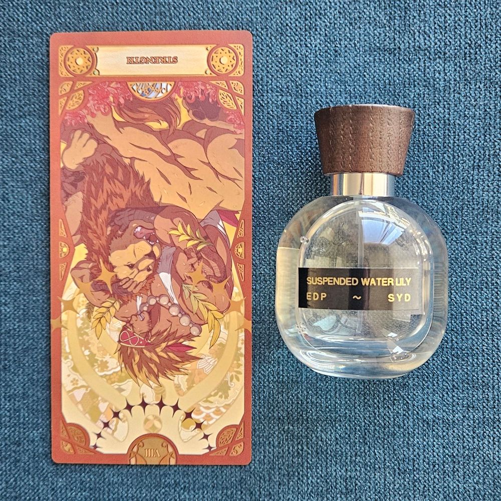 A reversed card VIII Strength sits next to a bottle of Suspended Water Lily by Syd Botanica, nose: Syd Buffman