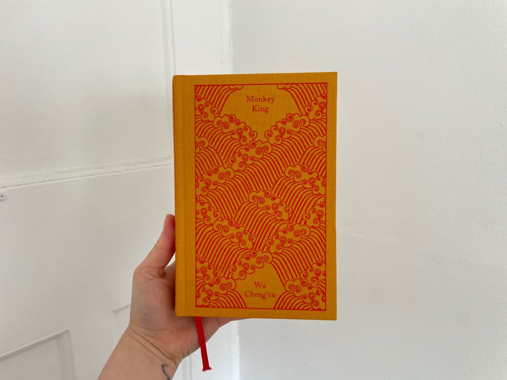 gab holds a penguin class book Monkey King with gold fabric and a cover with red outlines of waves 