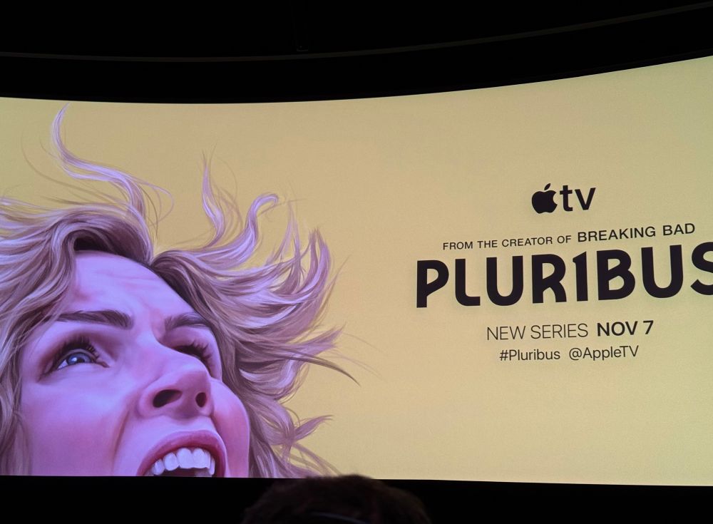 Ad for Pluribus on a curved screen. It features an artist’s closeup portrait of Rhea Seehorn, in character against a yellow background. About 3/4 of her head is visible. She’s looking up, her mouth open and expression troubled. Her hair is windblown. The ad reads From the creator of Breaking Bad. Pluribus, new series Nov. 7. The I in Pluribus is a 1.