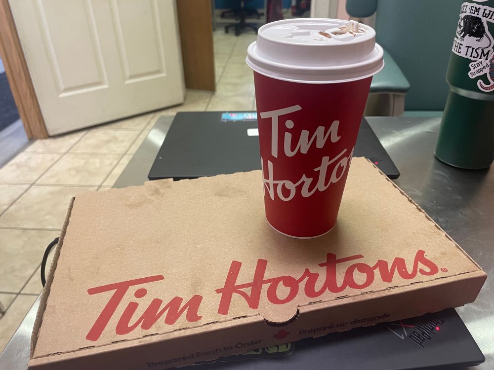 A coffee and pizza from Tim Hortons sits on a desk. (They are both pretty tasty in case you were wondering)