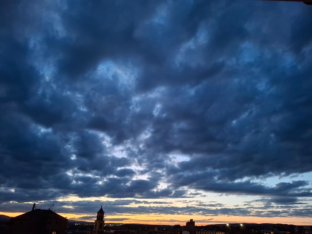 Atardecer con nubes azul oscuro entre un naranja y amarillo en el horizonte.