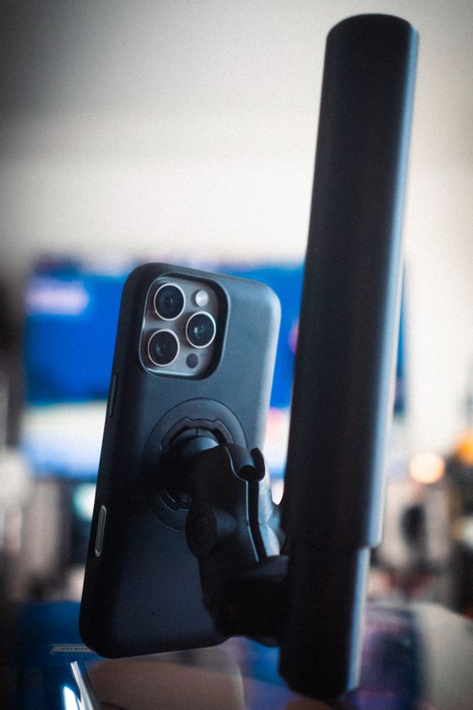 Shallow depth of field photo of a recent model iPhone Pro in a Quad Lock case with an attached RAM mount adapter and arm connected to a black cylindrical antenna about 1.5x the height of the phone.
