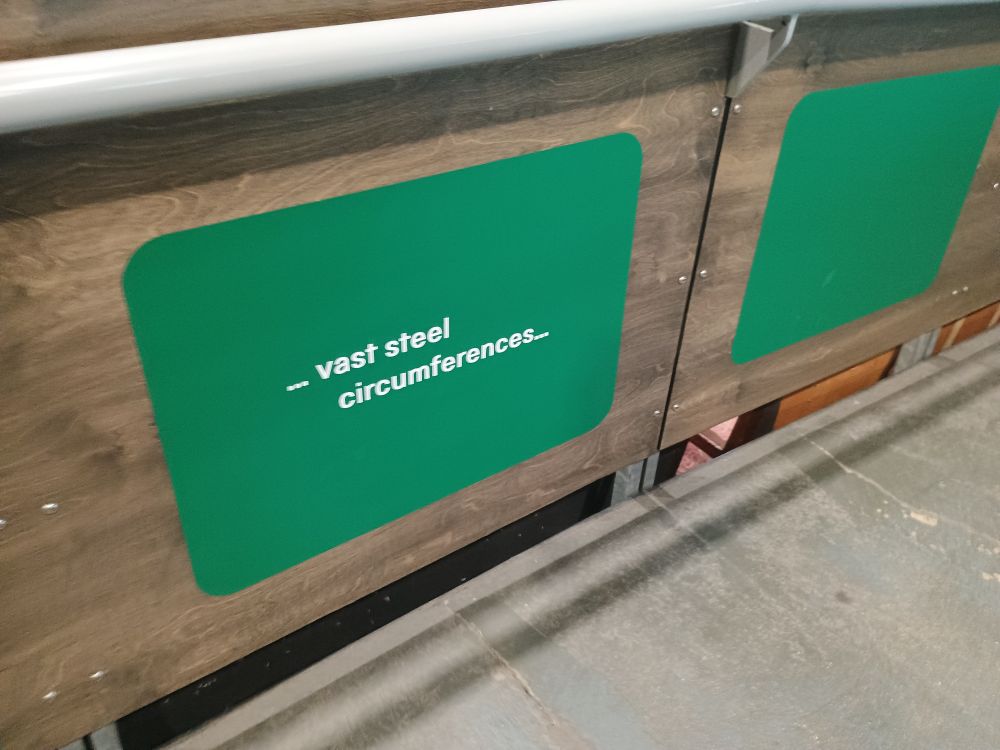 A green sign with white text at an exhibit at the National Train Museum in York that reads "... vast steel circumferences..."