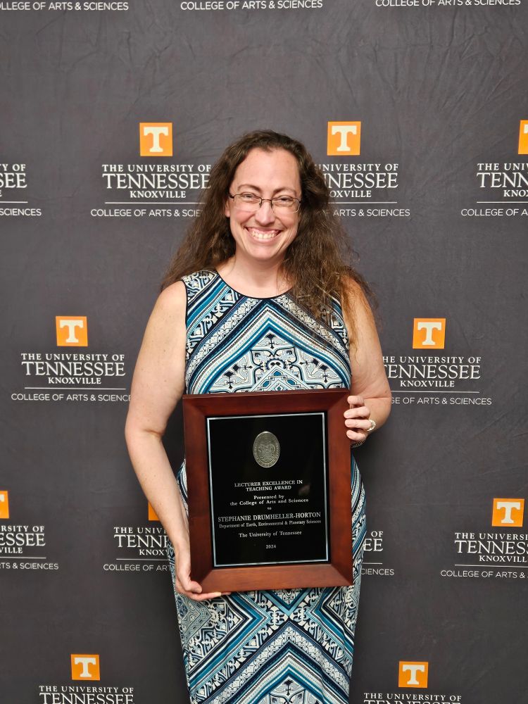 Stephanie Drumheller-Horton, in front of a UT logo backdrop, with a plaque for teaching in my hands