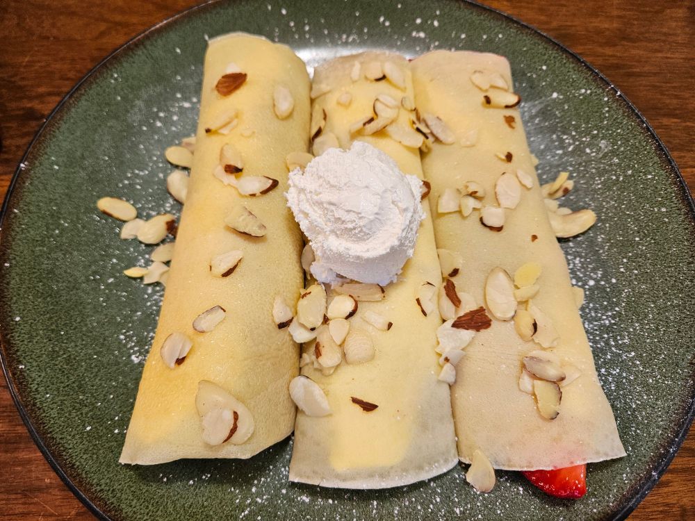 3 strawberry crepes on a plate with almonds on top