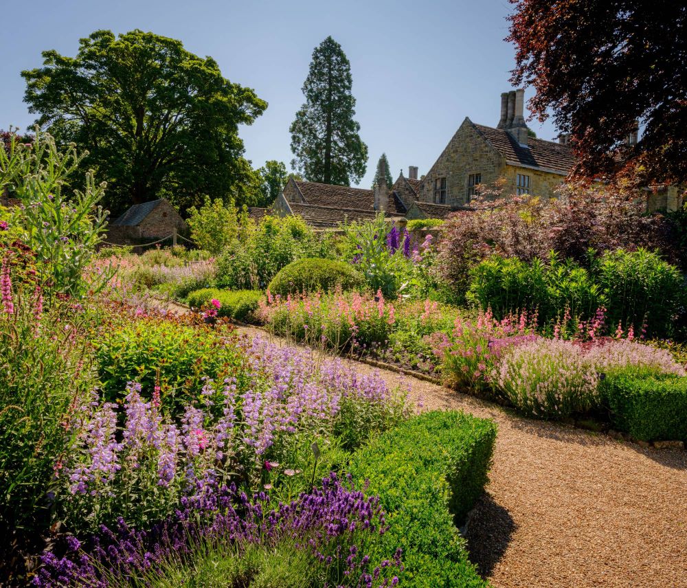 Wakehurst Place, Kew Gardens. A path with shrubbery and plants on either side leading up to a house