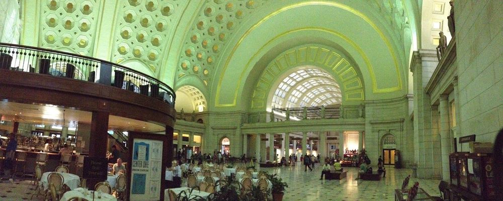 A picture showing the interior of the train station in Washington DC. There are tables set for dinner in the interior and people wandering around. The ceiling is illuminated in a greenish color.

The perspective is distorted because the picture was a panorama stitched from multiple images.